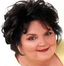 A woman with short, dark, curly hair smiles at the camera. She has fair skin, wears natural makeup with red lipstick, and is dressed in a light-colored top against a white background.