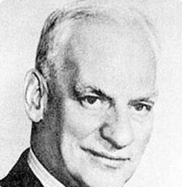 Black and white portrait of an older man with short, neatly combed white hair, wearing a suit and tie, and smiling slightly while looking forward.