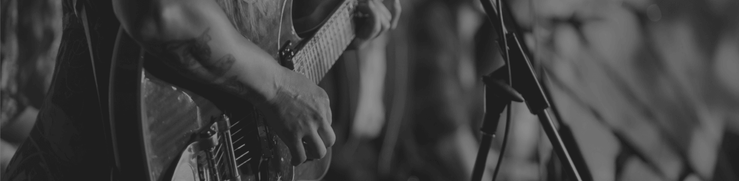 A close-up black and white shot of a guitarist's hands playing an electric guitar on stage near a microphone stand