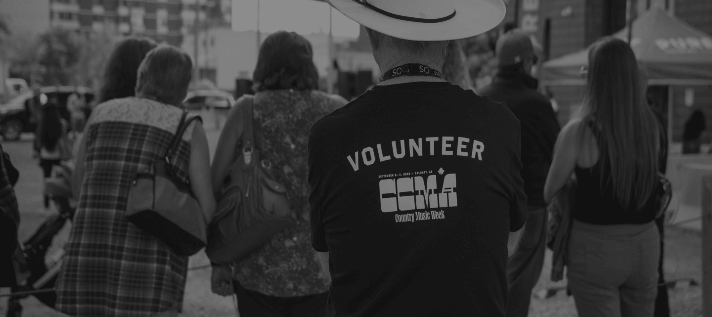 A person wearing a CCMA Country Music Week volunteer t-shirt walks among a crowd outdoors