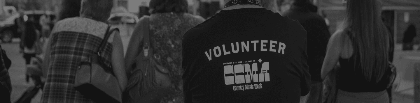 A person wearing a CCMA Country Music Week volunteer t-shirt walks among a crowd outdoors